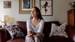 La Dra. Gisela Cánepa sentada en el mueble de su sala. Viste una blusa blanca y pantalón crema.