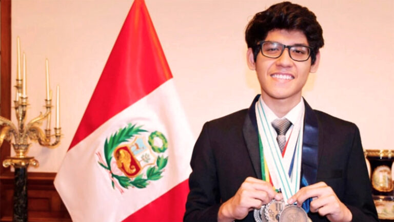 Estudiante joven con terno y medallas. A la izquierda de la imagen hay una bandera del Perú. Él sonríe, lleva pelo corto y lentes gruesos
