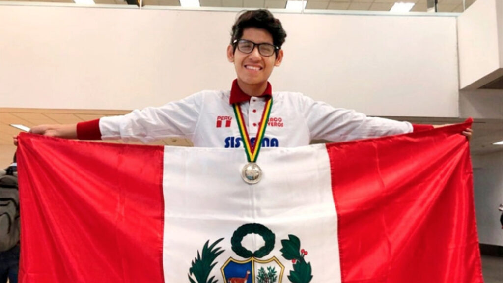 Estudiante joven sostiene una bandera del perú con los brazos abiertos. Lleva una medalla colgada del cuello