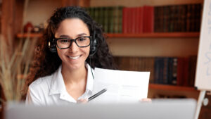 mujer joven usa lentes y está sentada frente a una laptop en clases virtuales