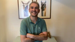 El profesor Ian Vázquez con polo verde, brazos cruzados. En el fondo un cuadro con dos llamas.