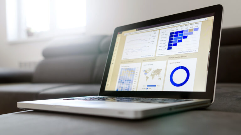 Fotografía de una laptop en cuya pantalla se muestran gráficos de barras y circulares de estilo financiero en tonos azules.