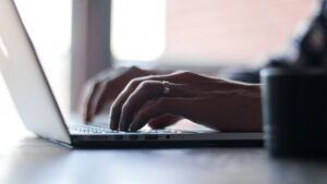 Una laptop con una vista desde el costado y un par de manos están tecleando sobre ella