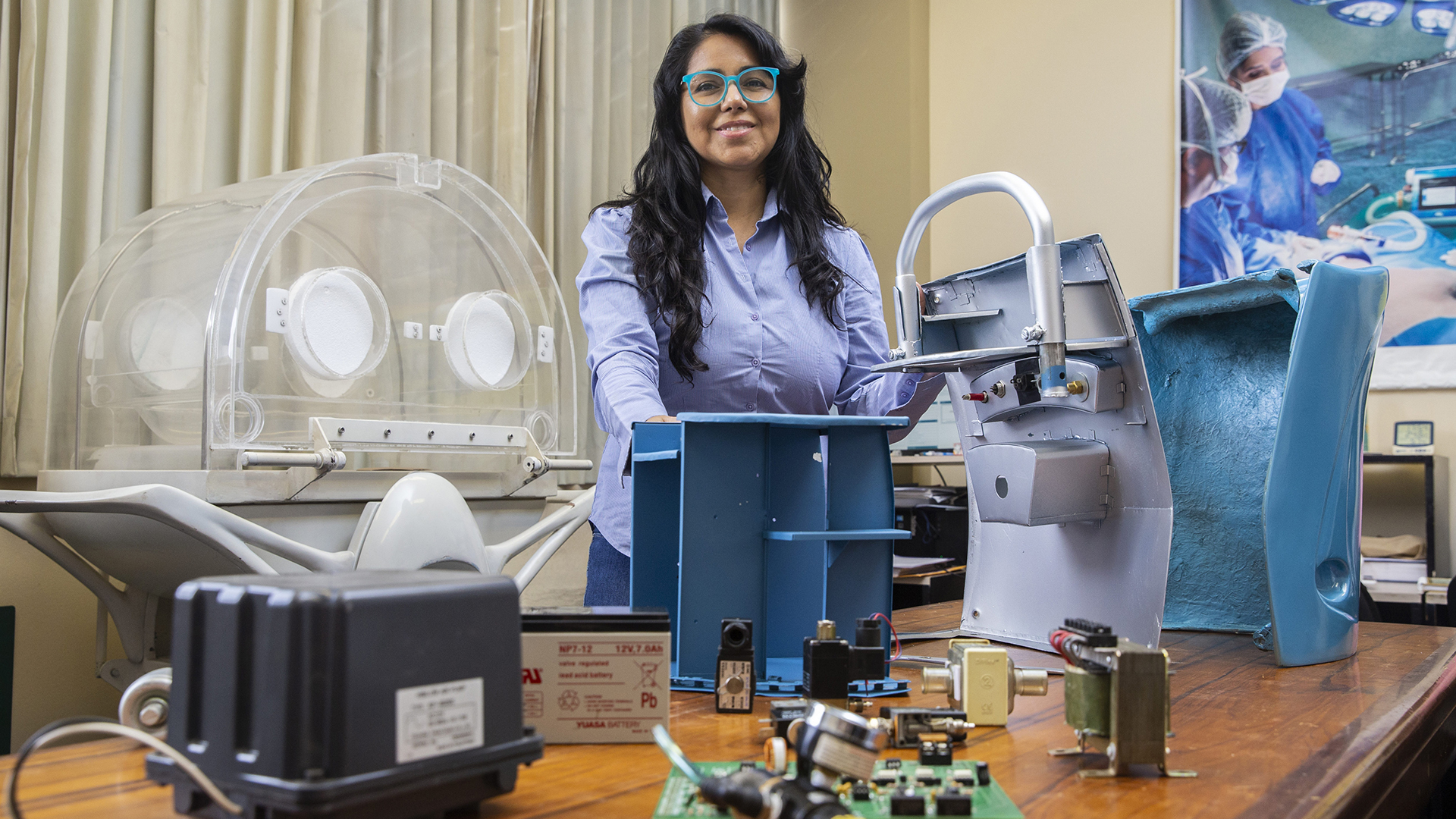 La inventora Consuelo Cano rodeada de distintas partes que componen un armázón portátil. Ella tiene camisa celeste y lentes de celeste encendido. Leeva el pelo largo y sonríe a la cámara.