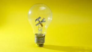 Imagen de un foco y adentro tiene unas herramientas. el fondo es amarillo