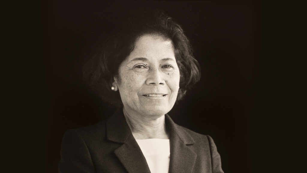fotografía en blanco y negro de la profesora beatriz mauchi, una mujer de aprox 50 años en su retrato. Sonríe a la cámara ligeramente, lleva blusa blanca y saco negro.