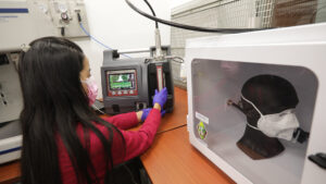 Mujer manipulando el equipo que evalúa la capacidad de filtración de las mascarillas.