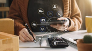 Fotocomposición: se ve una chica con una libreta y una calculadora en una mesa, en la mano tiene un celular. Del celular salen logos de búsqueda y conexión digital