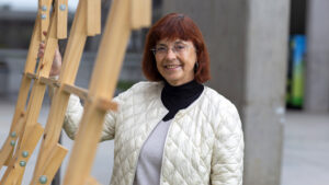 Foto de la antropóloga Dolors Comas, especiailsta en cuidado. es una señora de 50+ años, de tex blanca y cabello rojo que mira sonriendo ala cámara. lleva casaca blanca, blusa de cuello alto negro.
