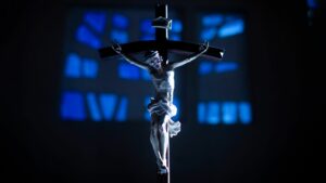 Fotos de semana santa en la PUCP: Crucijifo plateado con detalles, con una iluminación azul que pasa a través de vitrales.