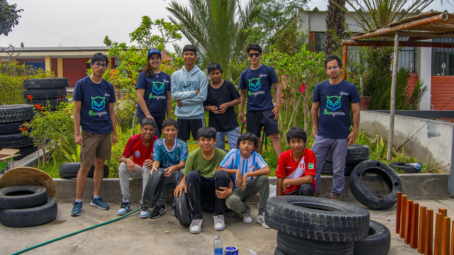 Ganadores del Educactón PUCP 2022 con estudiantes de colegio en san bartolo. están en un jardín trabajando con llantas para reutilizarlas