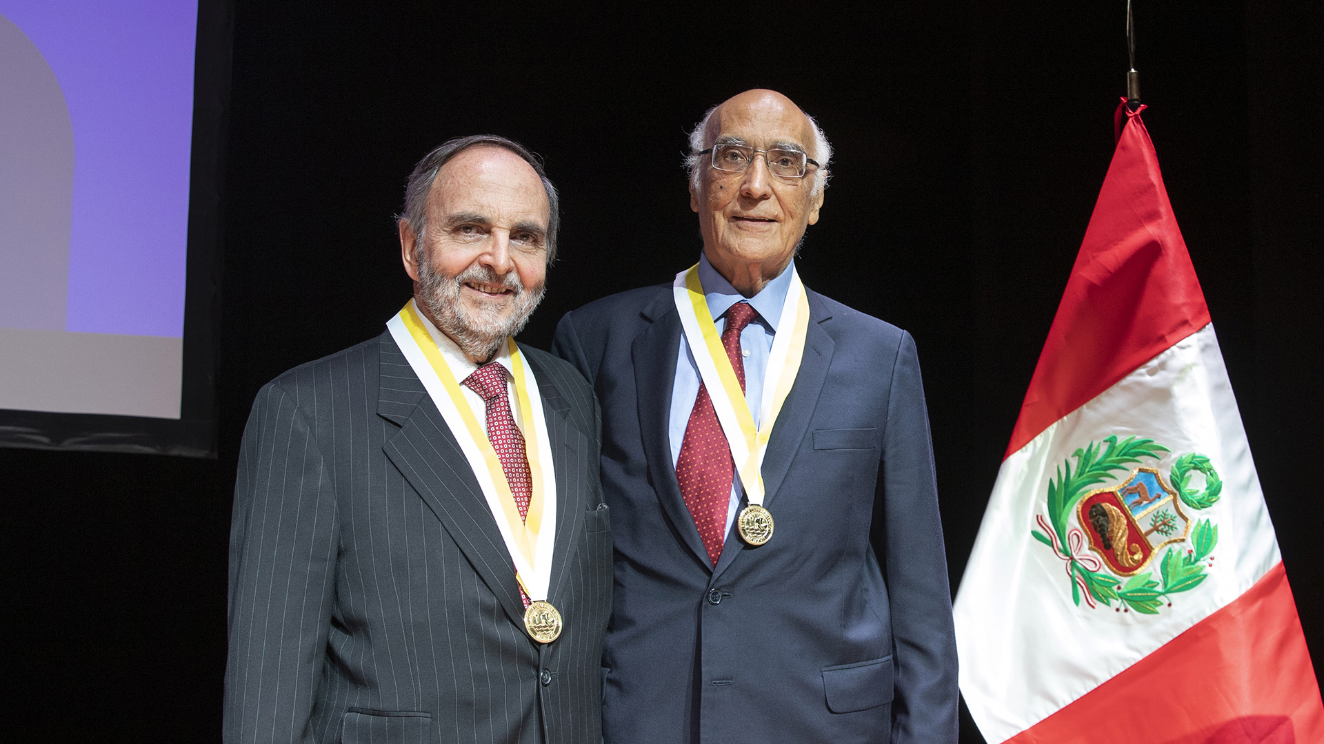 profesores eméritos javier de belaúnde y humberto medrano, con sendas medallas y en terno, sonríen a la cámara,