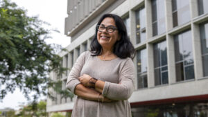 Retrato de la profesora Maria Eugenia Ulfe quien ganó una beca de investigación de The British Academy. En la foto ella posa con los brazos cruzados frente al edificio de Ciencias Sociales en el campus PUCP.
