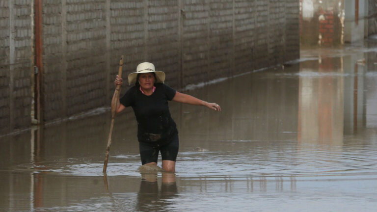 foto del fenómeno del niño: una calle inundada y una señora caminando con el agua hasta las rodillas, ayudada con un bastón.