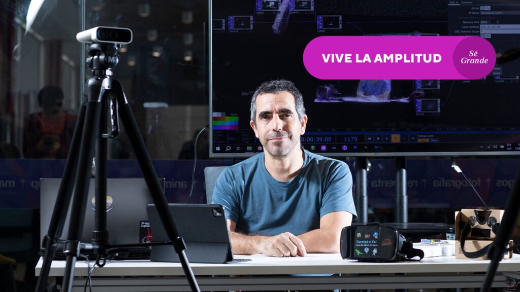Andrés León Geyer: profesor de aprox 40 años sentado detrás de una computadora, cámaras y delante de una pantalla grande con datos. a su costado dice "vive la amplitud/sé grande"