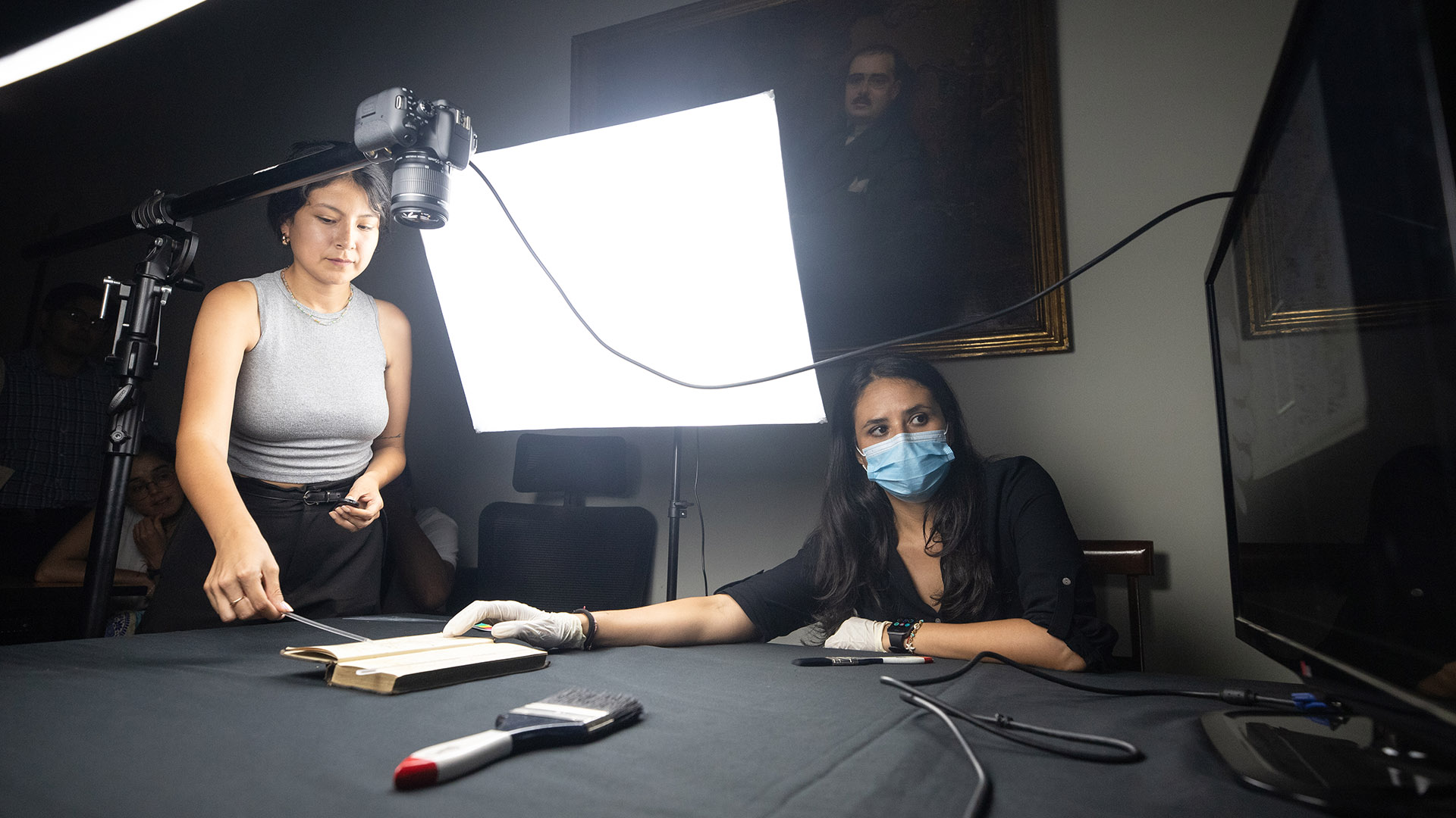 Dos especialistas con mascarillas, guantes e implementos usan el scanner espacial para digitalizar un cuaderno de Cavero sobre una mesa.