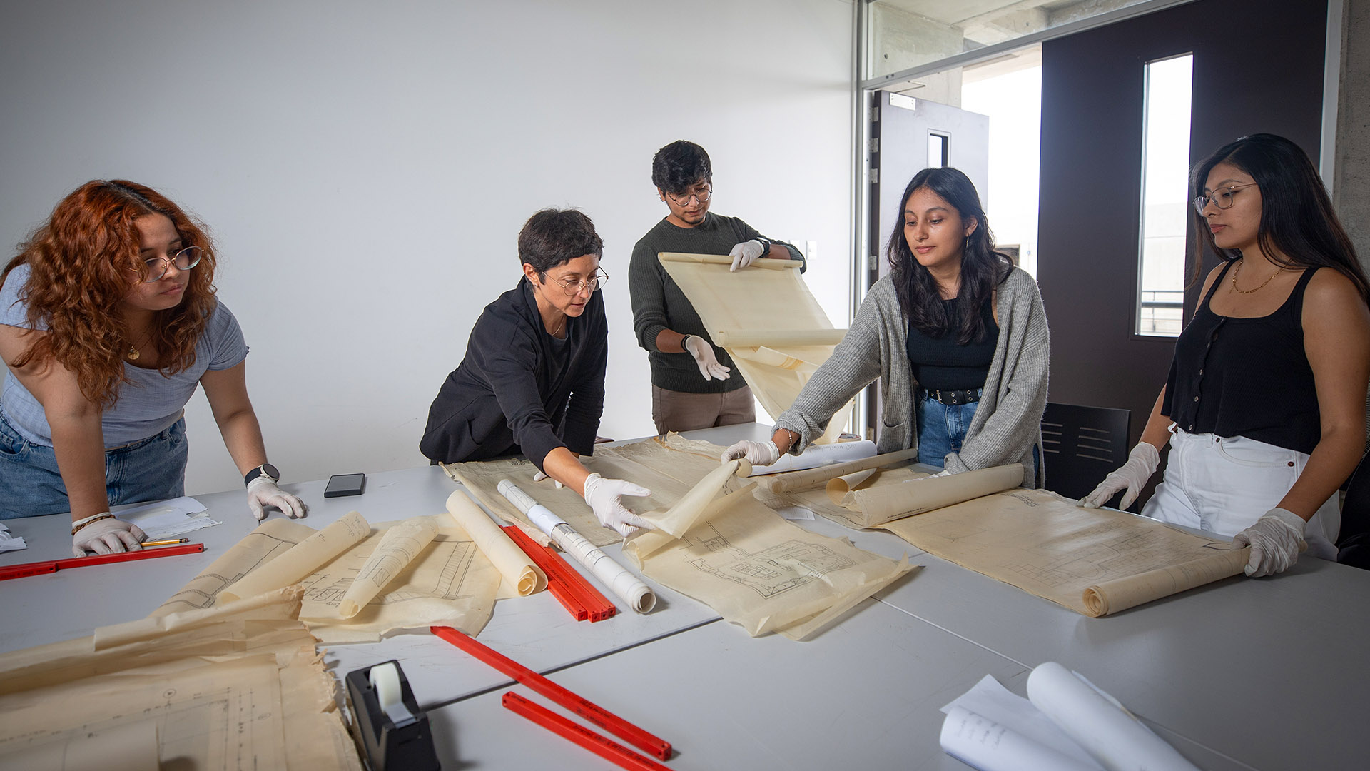 tres personas frente a una mesa manipulando con cuidado planos.